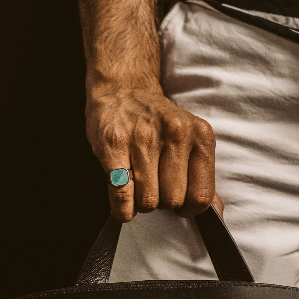 A man holding a handbag with a turquoise ring on it.