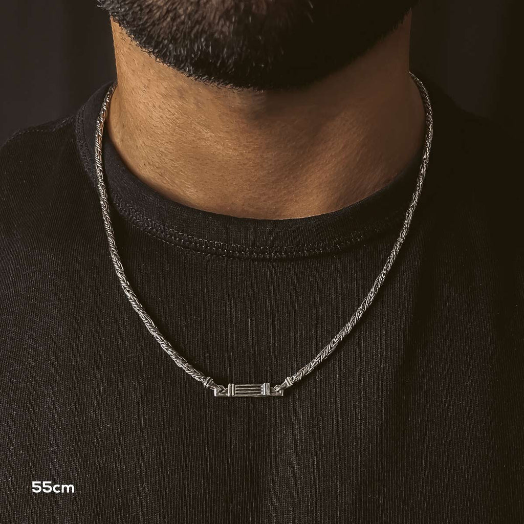 A man with a beard wearing a silver necklace.