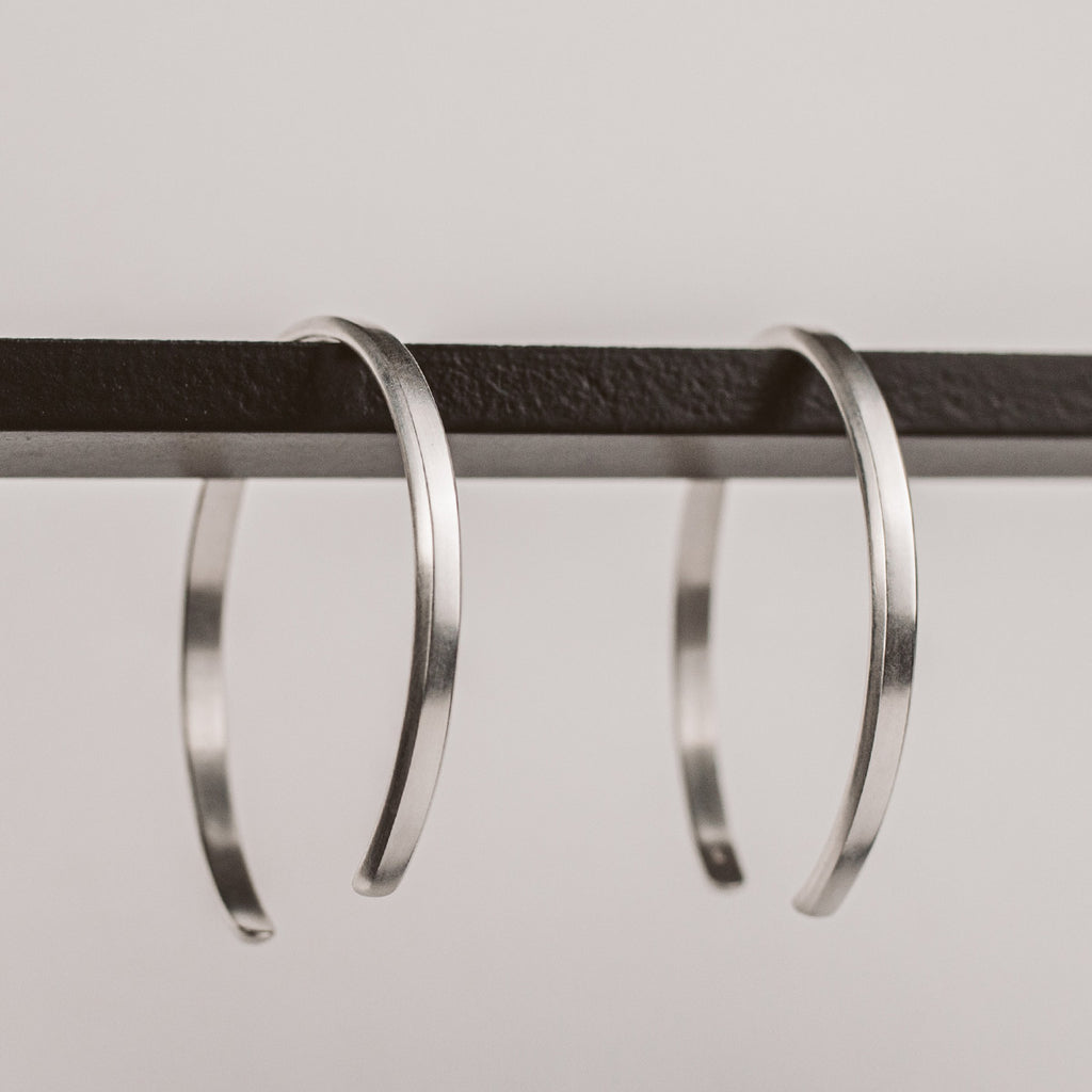 A pair of silver hoop earrings hanging from a rod.