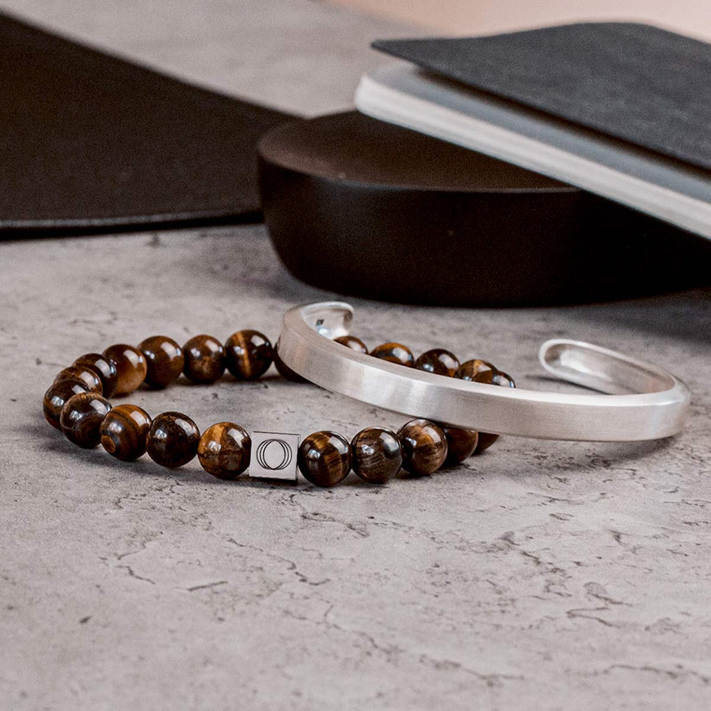 A notebook and a pair of tiger eye bracelets rest on a desk.
