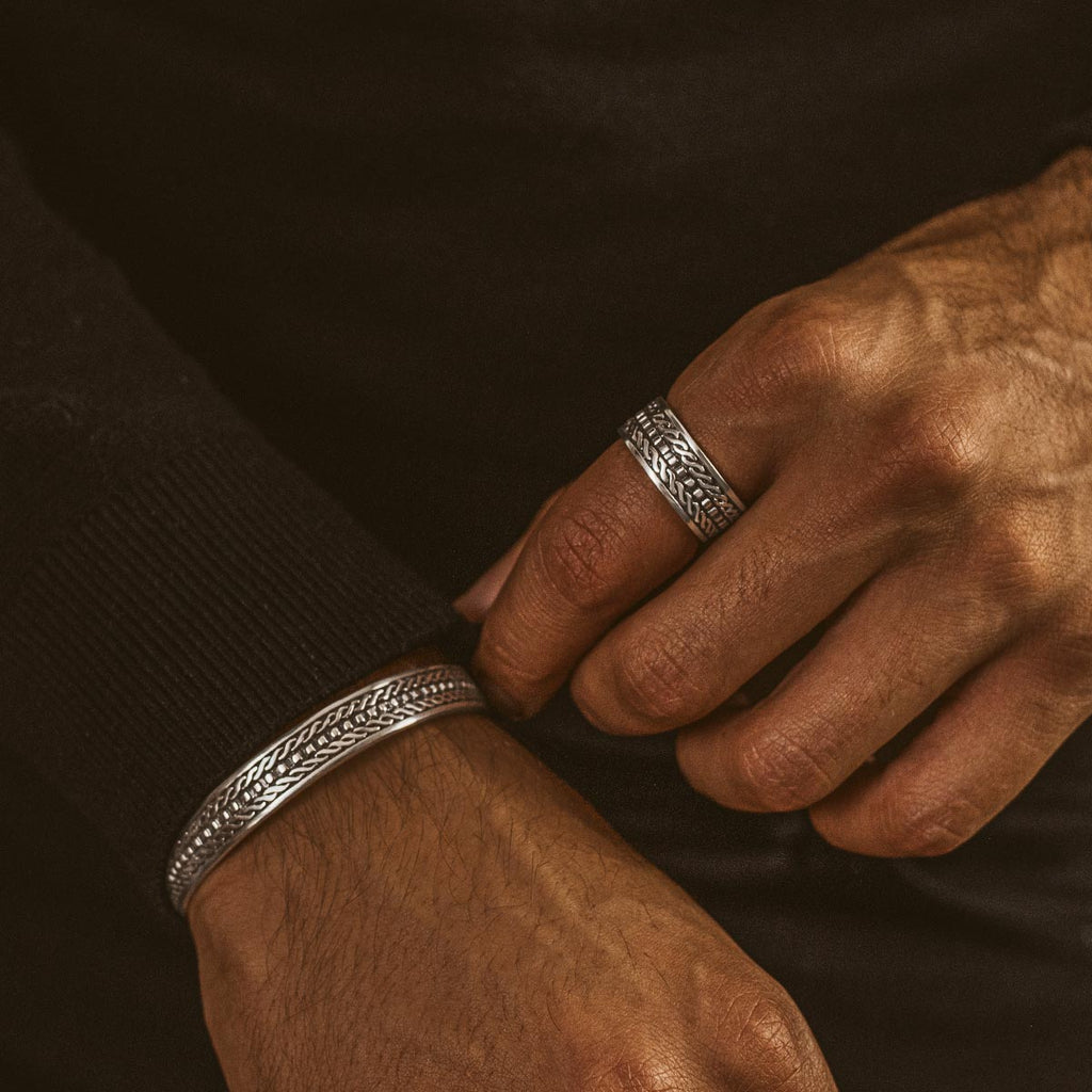 Een man draagt een zilveren ring met een patroon erop.