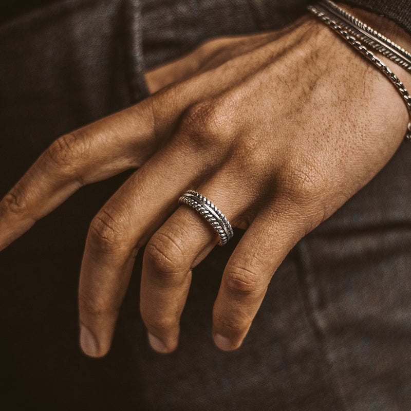 Ein gravierter Zahir Herrenring aus Sterling Silber mit Federdesign und das Ninetwofive-Manschettenarmband schmücken die Hand eines Mannes.