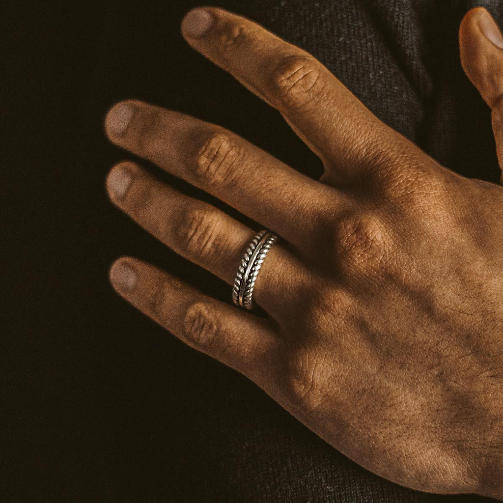 Een gegraveerde Zahir - Sterling Zilveren Veren Ring 6mm voor hem, die de hand van een man siert.