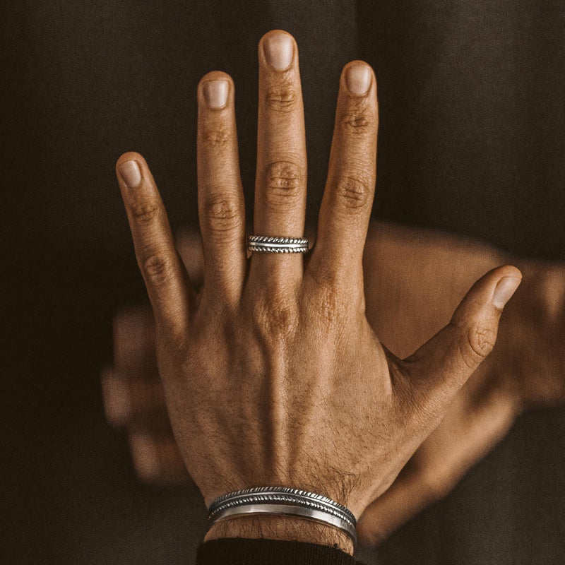 Ein gravierter Zahir Herrenring aus Sterling Silber am Ringfinger, dazu trägt er ein Armband.