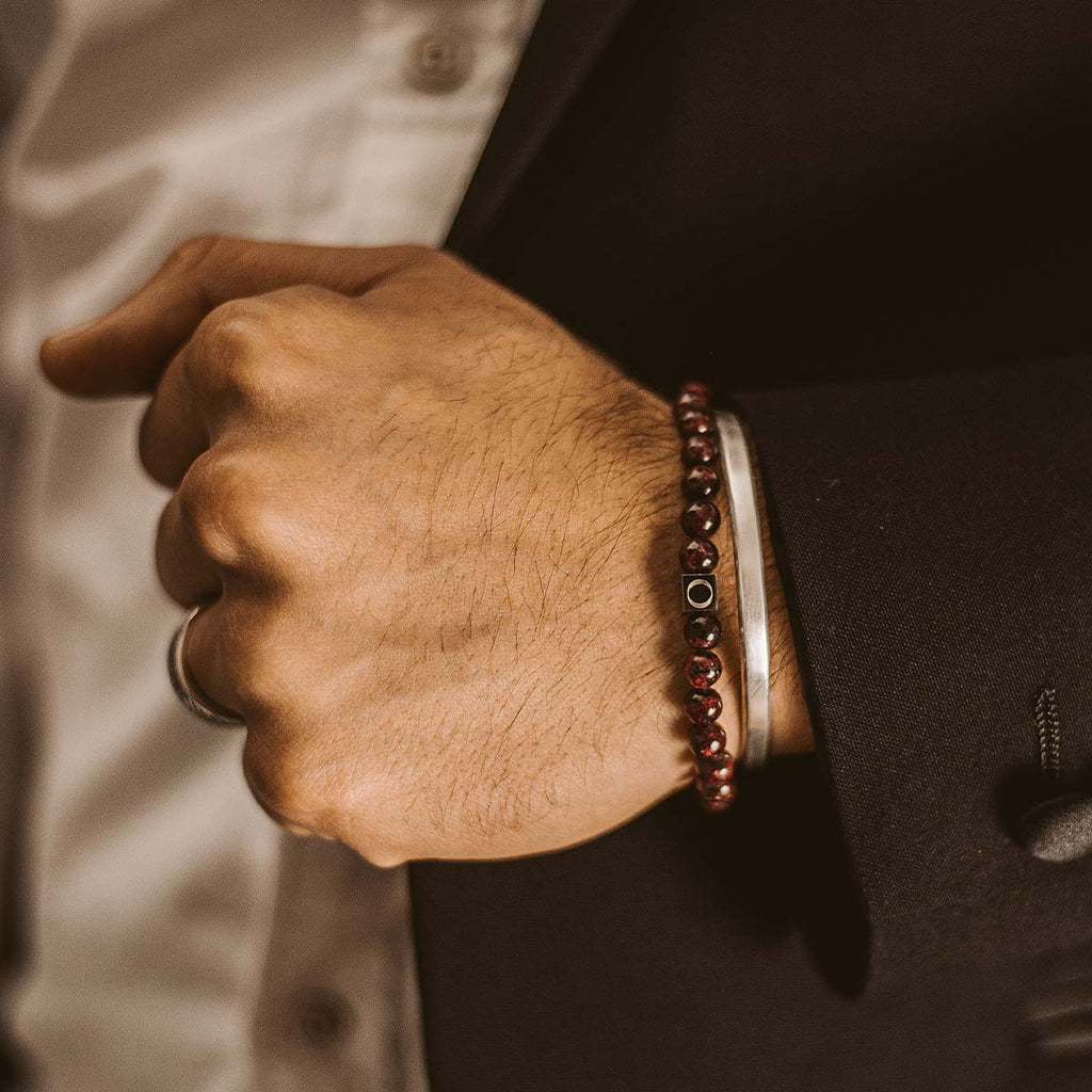 A man in a suit is wearing a red bracelet.