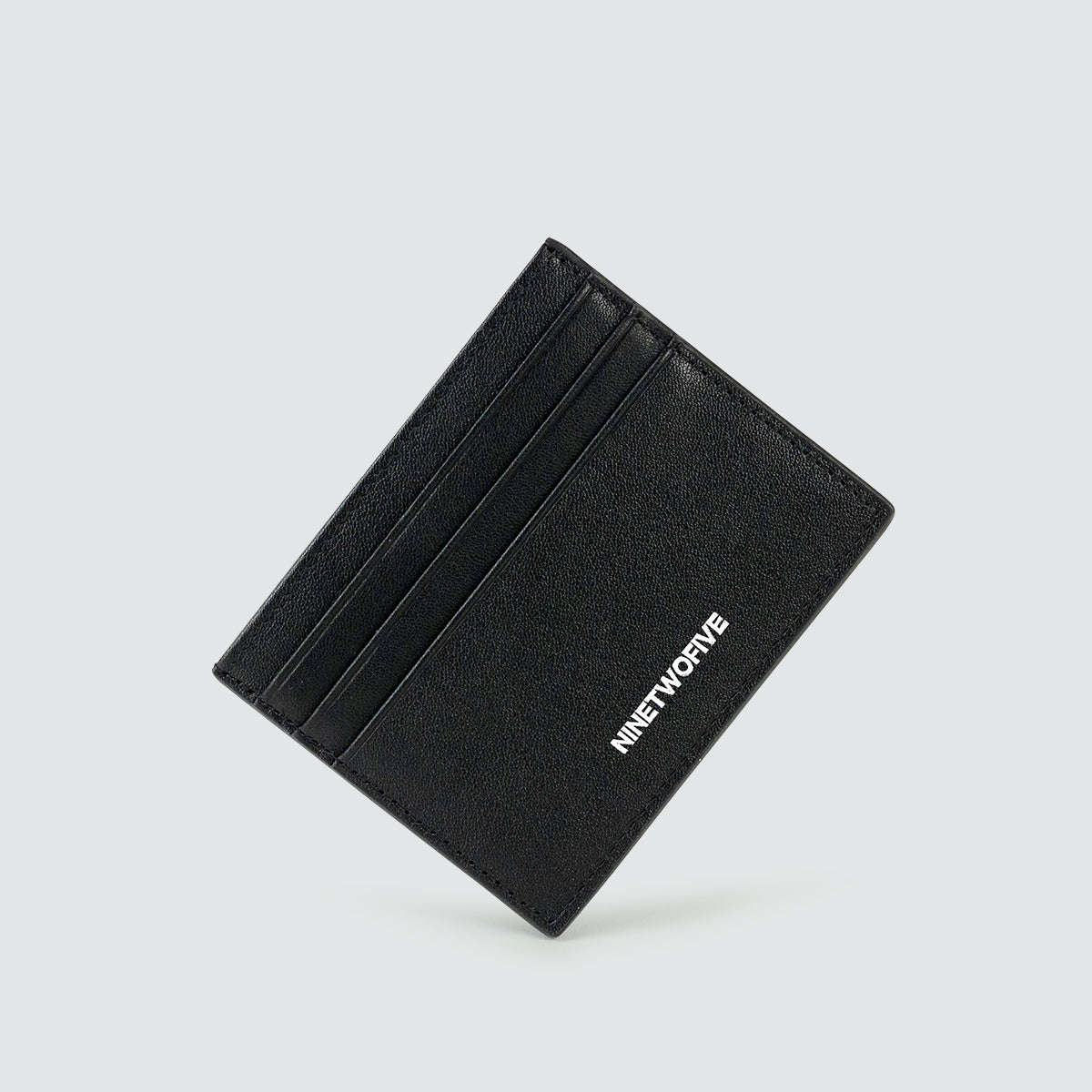 Schuine weergave van de gratis portemonnee van echt zwart leer voor heren, met de eersteklas matte afwerking en kwaliteitsstiksels. Ninetwofive.