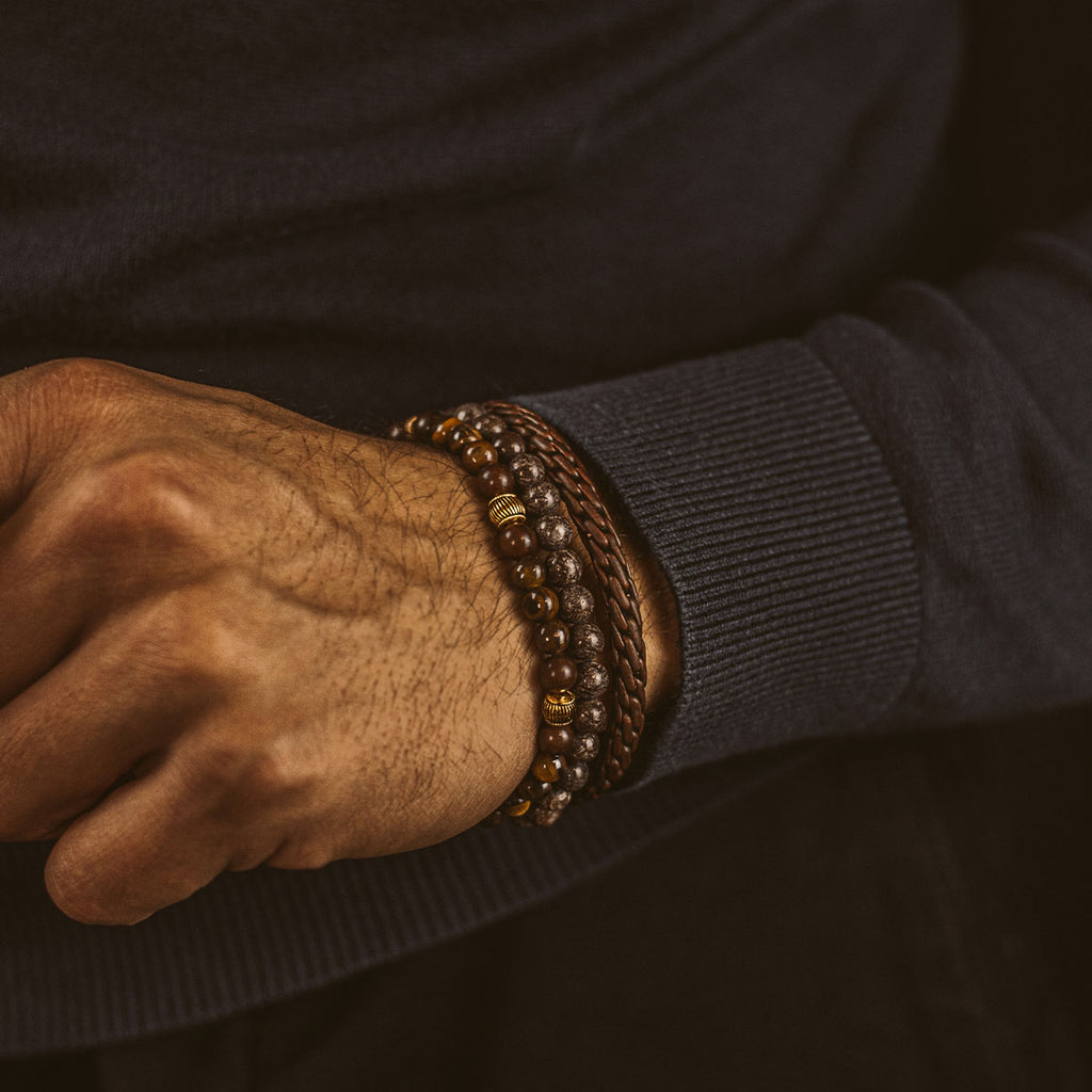 Een man draagt de Kaliq - Verstelbare Tijgeroog Kralen Armband in Goud 6mm.