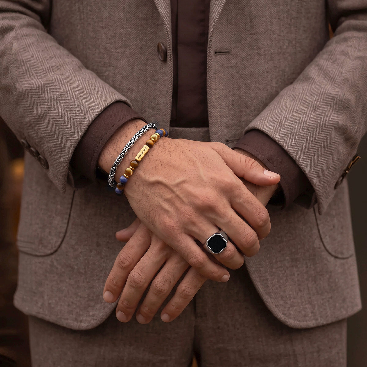 Man in a brown suit with hands crossed, wearing the Halloween Treat tiger eye beaded bracelet