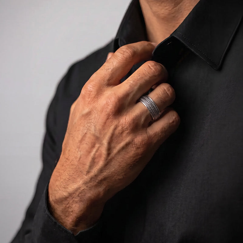 Man adjusting the collar of his black shirt while wearing the Hani herringbone spinner ring