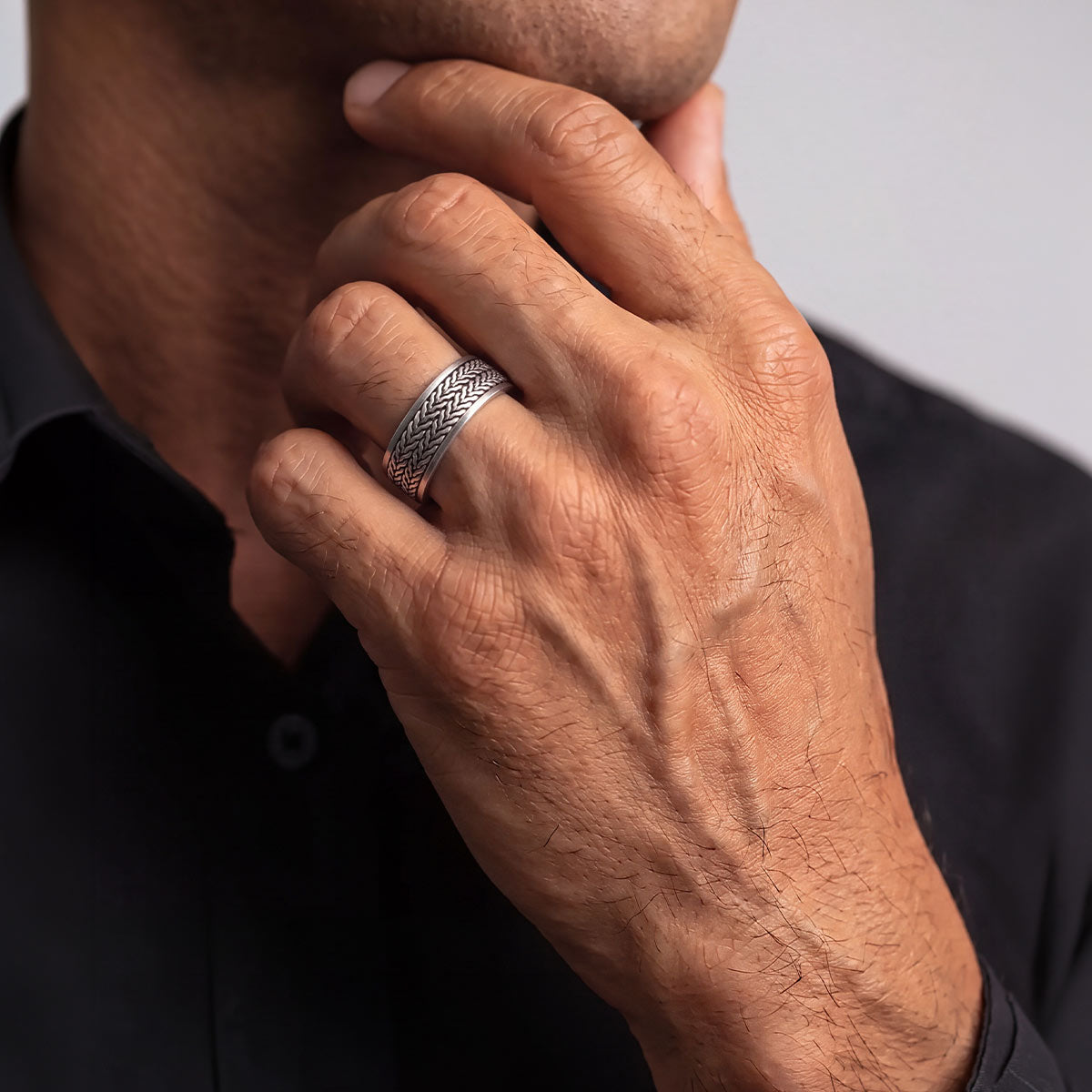 Man in a black shirt wearing the Hani silver spinner ring, hand resting at his chin