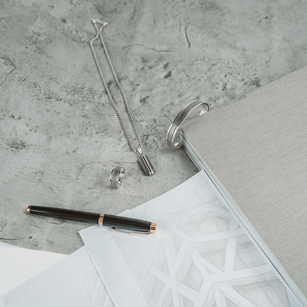 Kaliq herenarmband, -ring en -hanger van Ninetwofive met schetspapier, een boek en een vette pen. 