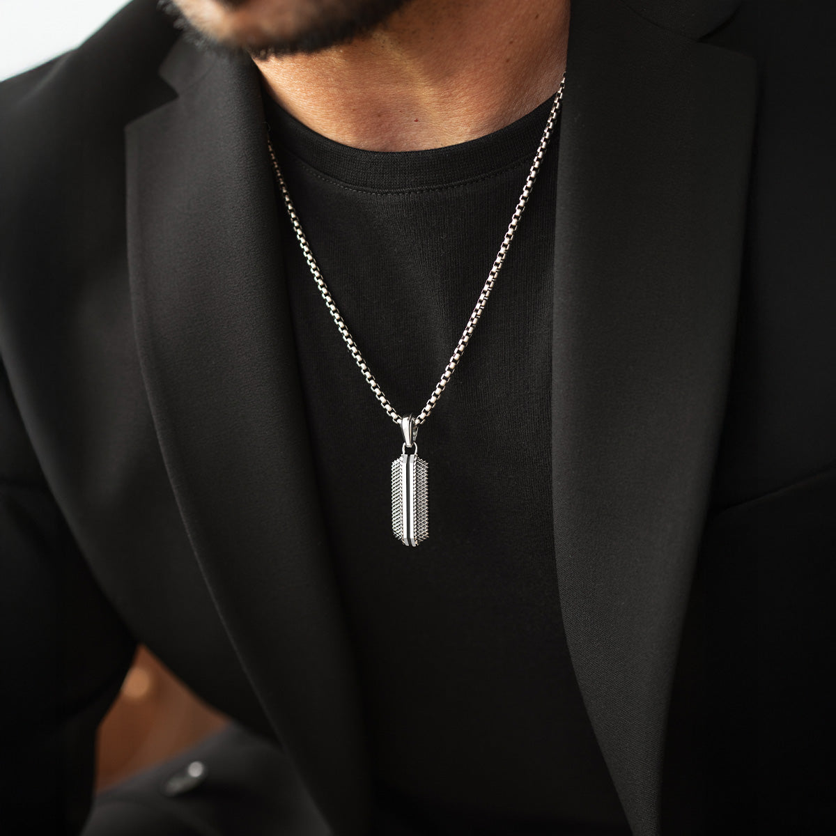 Close-up of Kaliq oxidised sterling silver pendant with chain, worn with a black blazer. Ninetwofive
