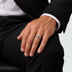 Seated man in a black suit wearing the Latif braided band ring, hand resting on his knee