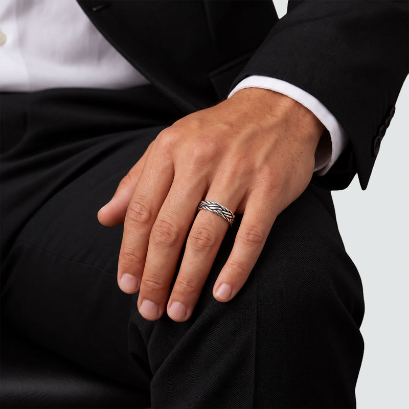 Seated man in a black suit wearing the Latif braided band ring, hand resting on his knee