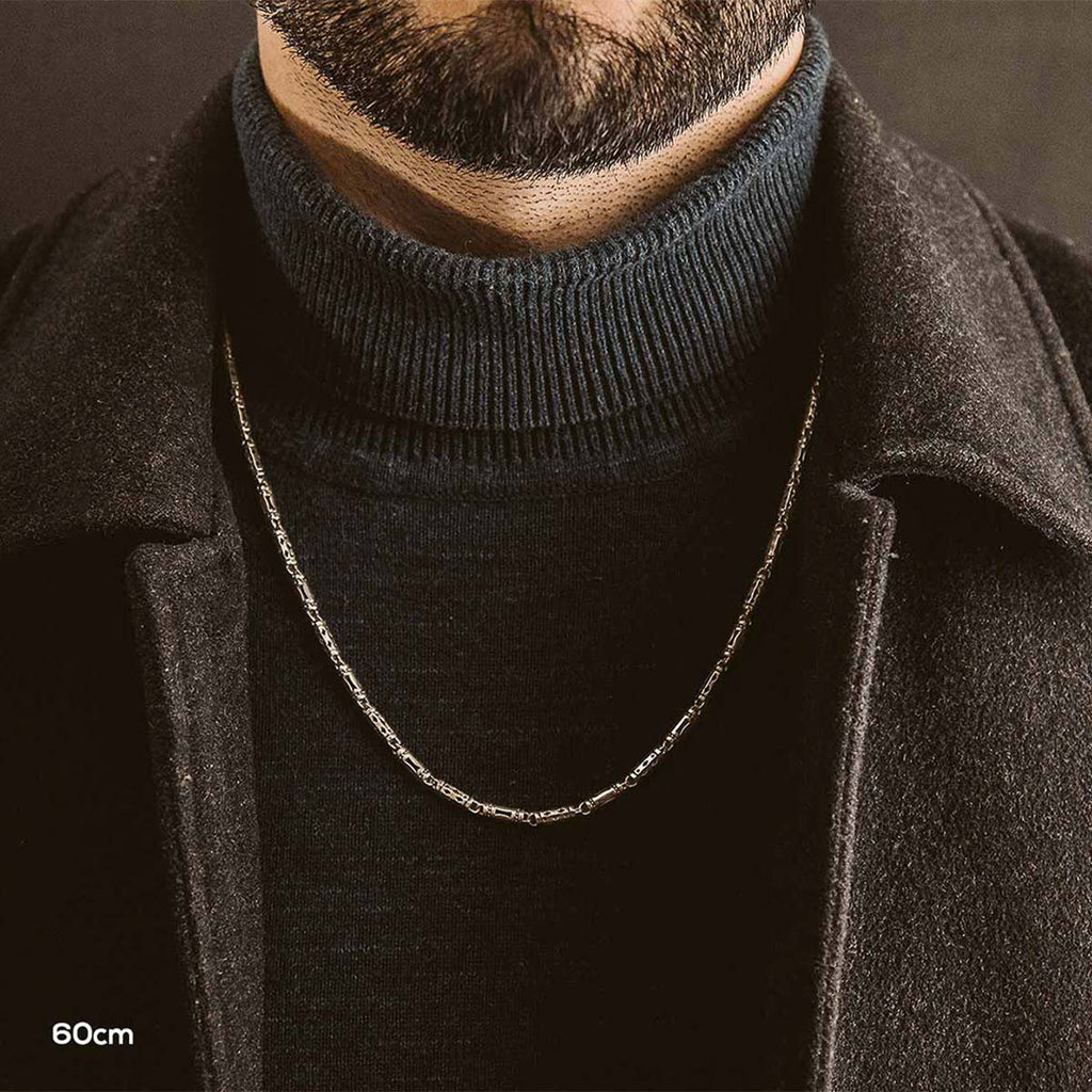 A man wearing a black sweater and chain.