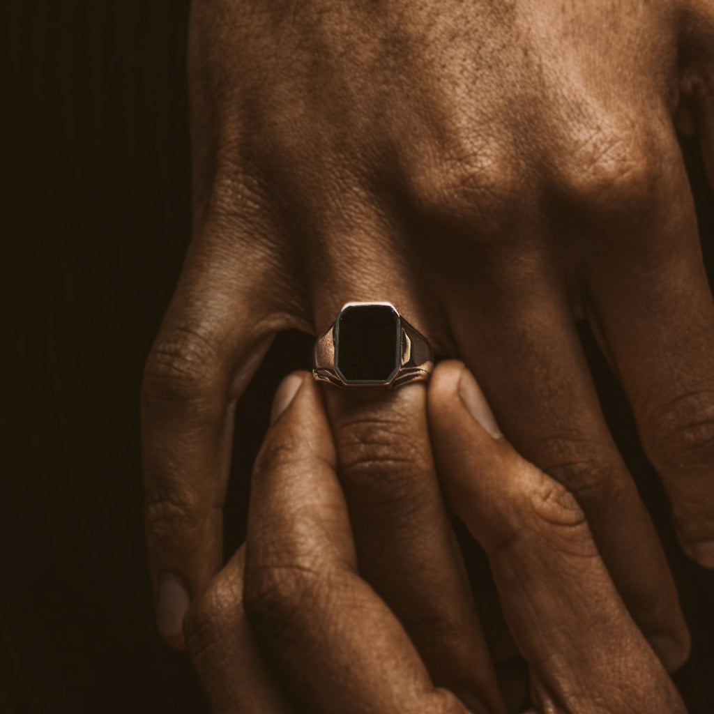 A man's hand holding a black onyx signet ring.