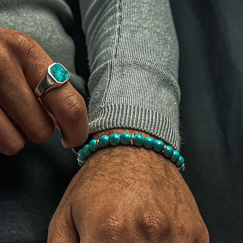 Man in grijze trui draagt de Nuri heren kralenarmband met turkoois en een sterling zilveren zegelring.