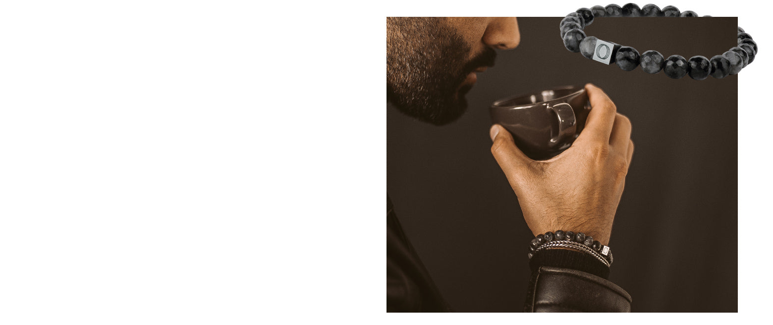 Man wearing black beaded bracelets while holding a mug from Ninetwofive. 