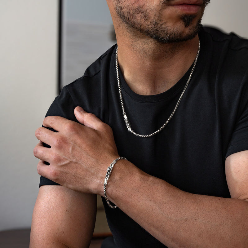 Ein Mann in einem schwarzen Hemd mit einem silbernen Box-Chain-Armband und einer Box-Chain-Halskette.