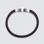 A dark brown braided leather bracelet with a silver-toned metal clasp featuring a textured geometric pattern, shown on a light gray background.