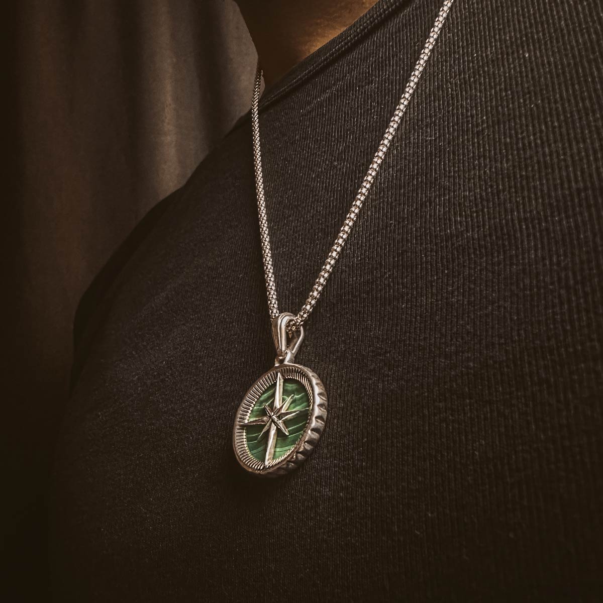 Un homme portant un compas Safar - Sterling Silver Malachite Compass Pendantif avec un trèfle vert dessus.
