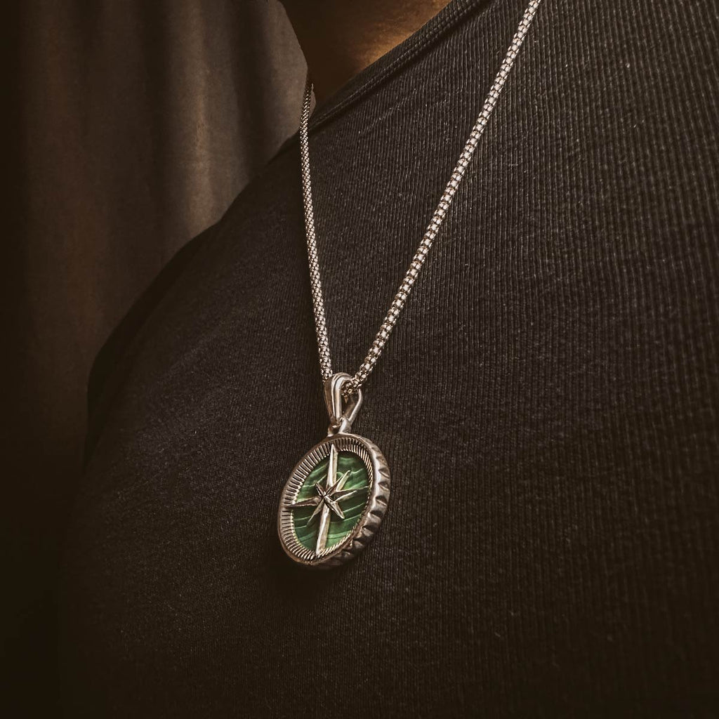 A man wearing a Safar - Sterling Silver Malachite Compass Pendant with a green shamrock on it.