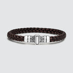 A dark brown braided leather bracelet with a silver-toned metal clasp featuring a central rectangular inlay, photographed on a light gray background.