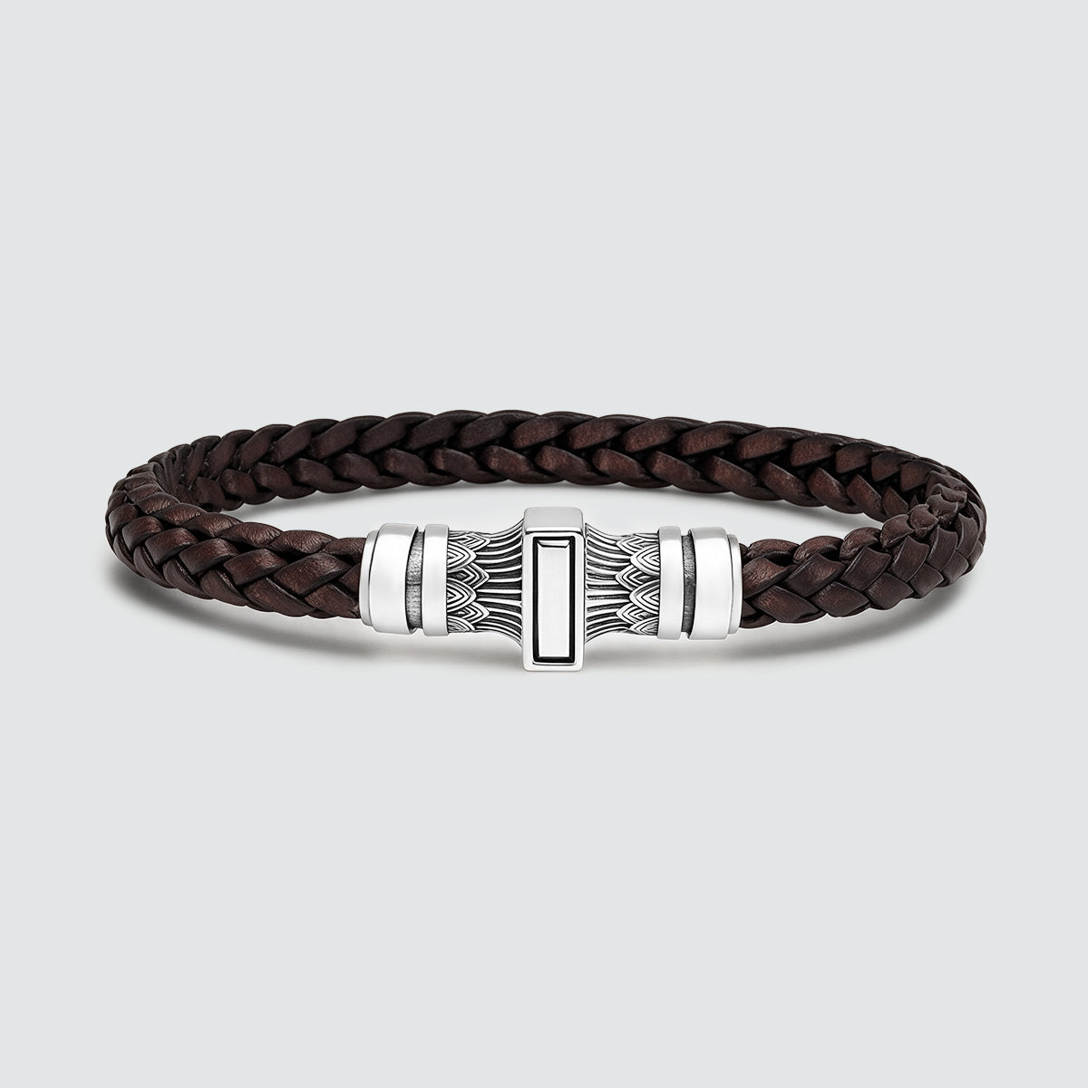 A dark brown braided leather bracelet with a silver-toned metal clasp featuring a central rectangular inlay, photographed on a light gray background.