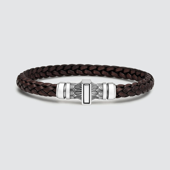 A dark brown braided leather bracelet with a silver-toned metal clasp featuring a central rectangular inlay, photographed on a light gray background.