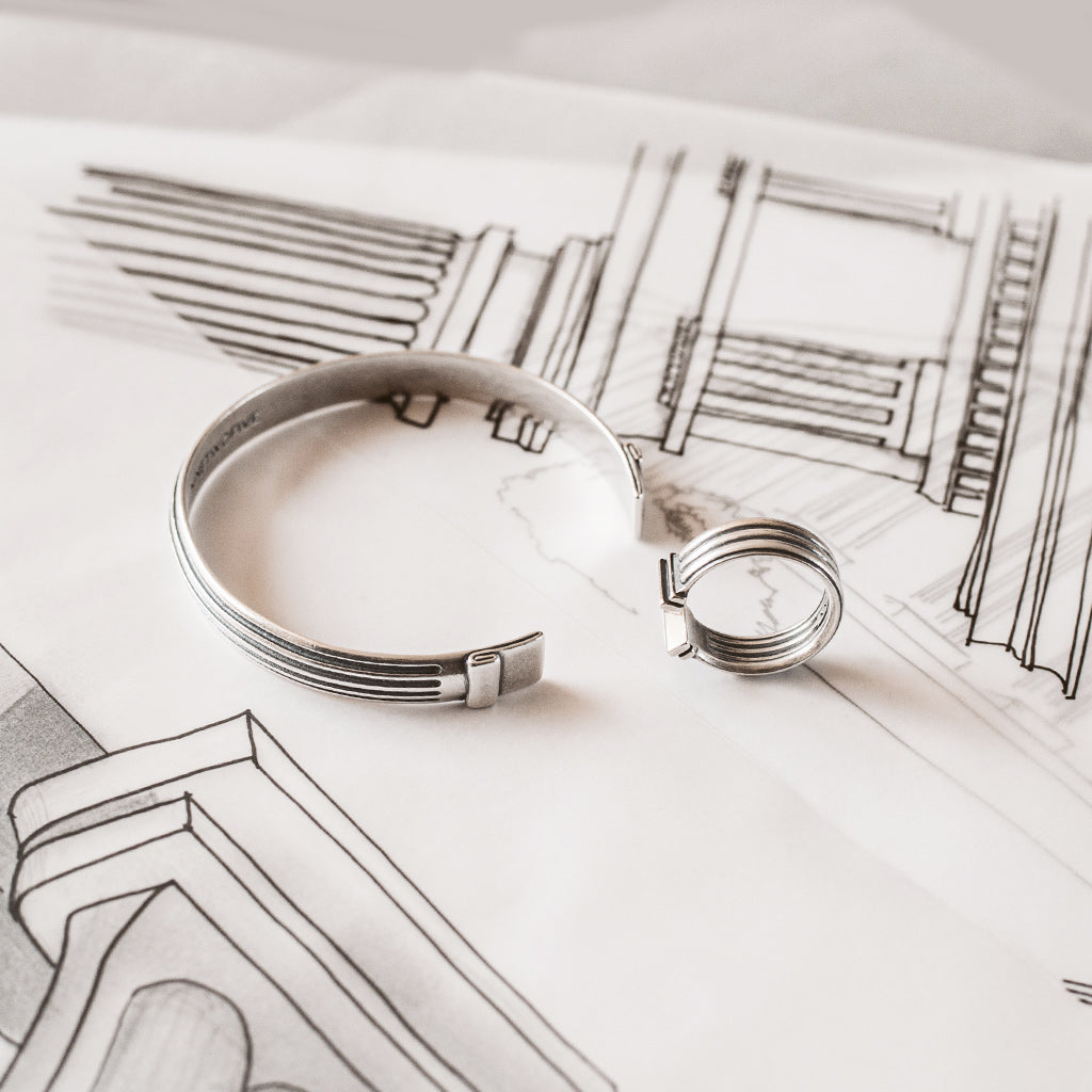 A silver cuff laying on a drawing.