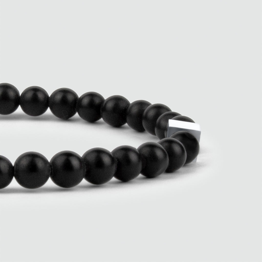 Een Aswad - Mat Zwarte Kralen Armband 6mm gemaakt met zwarte onyx stenen op een witte achtergrond.