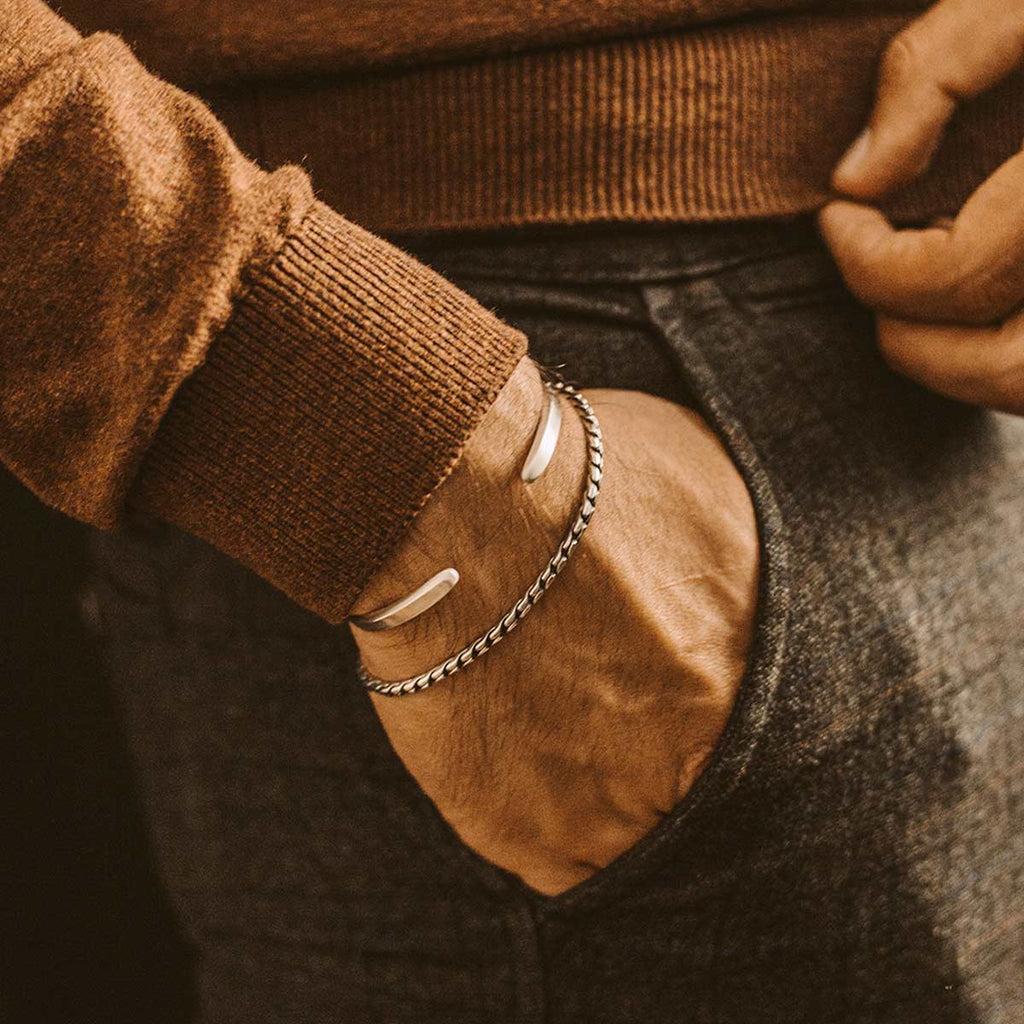 A man wearing a pair of silver bracelets.