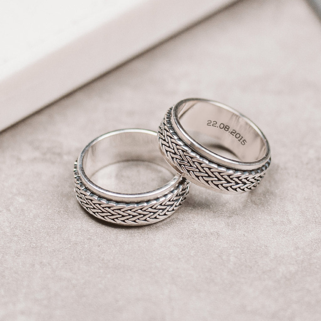 Two silver rings with braided designs are placed on top of a table.