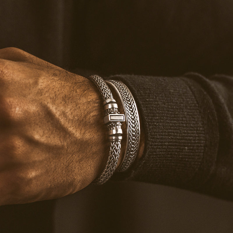 A man's wrist with Mirza sterling silver braided bracelet and a cuff by Ninetwofive. 