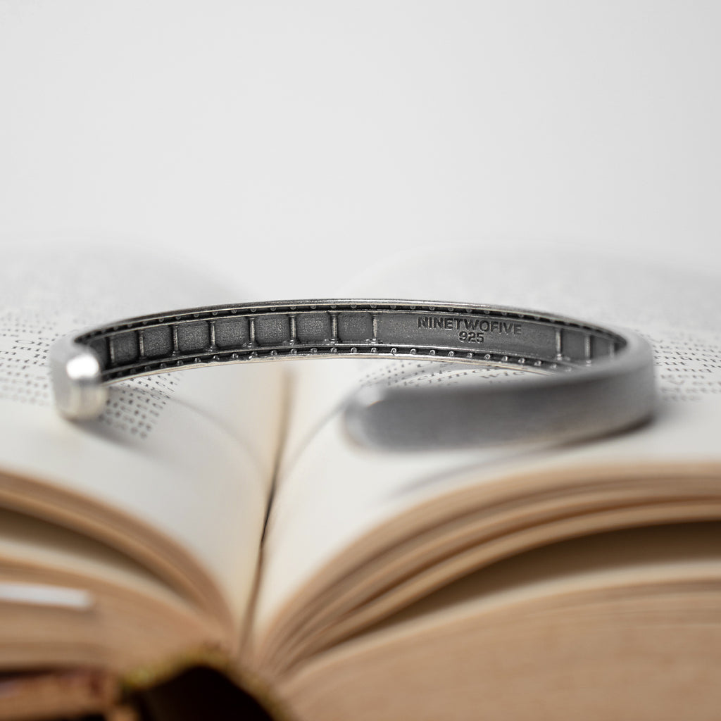 A silver cuff bracelet sitting on an open book.