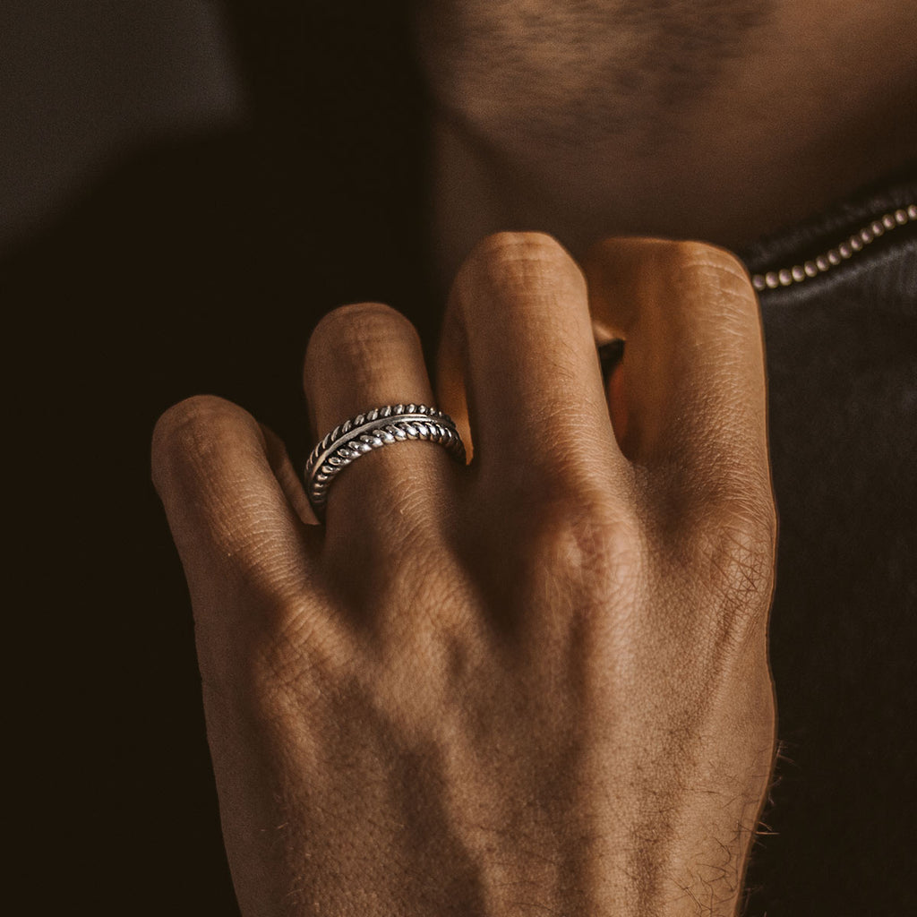 A man donning a Zahir - Sterling Silver Feather Ring 6mm with engraved design.