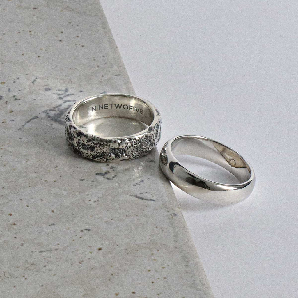 A pair of silver wedding rings on a marble surface.