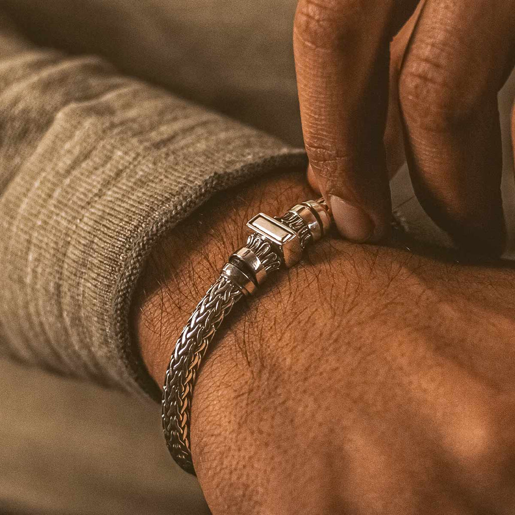 A man is putting on a silver bracelet.