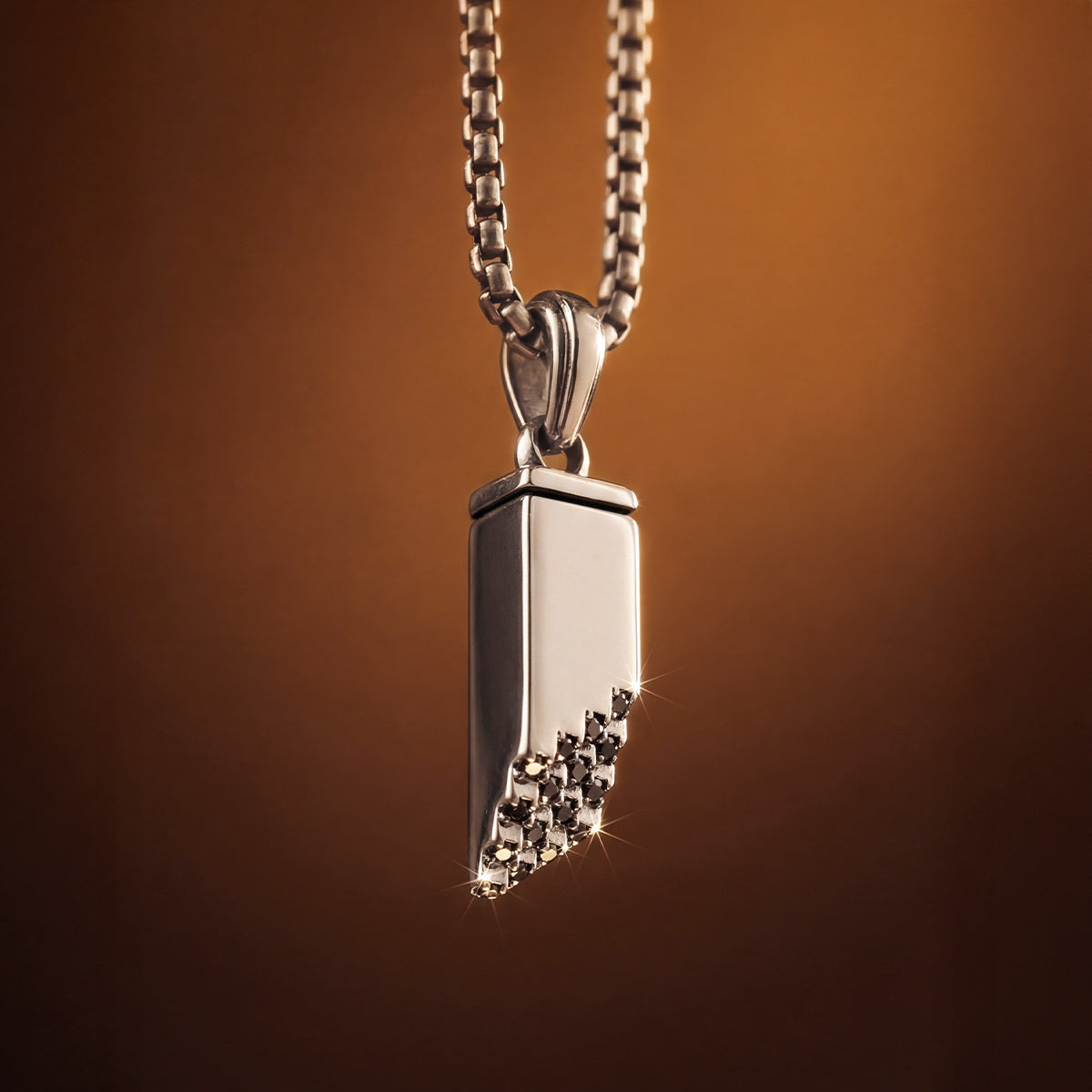 Ein silberner Herrenanhänger im Muqarnas-Stil mit schwarzen Diamanten von Ninetwofive vor einem warmen Goldhintergrund – Nahaufnahme.