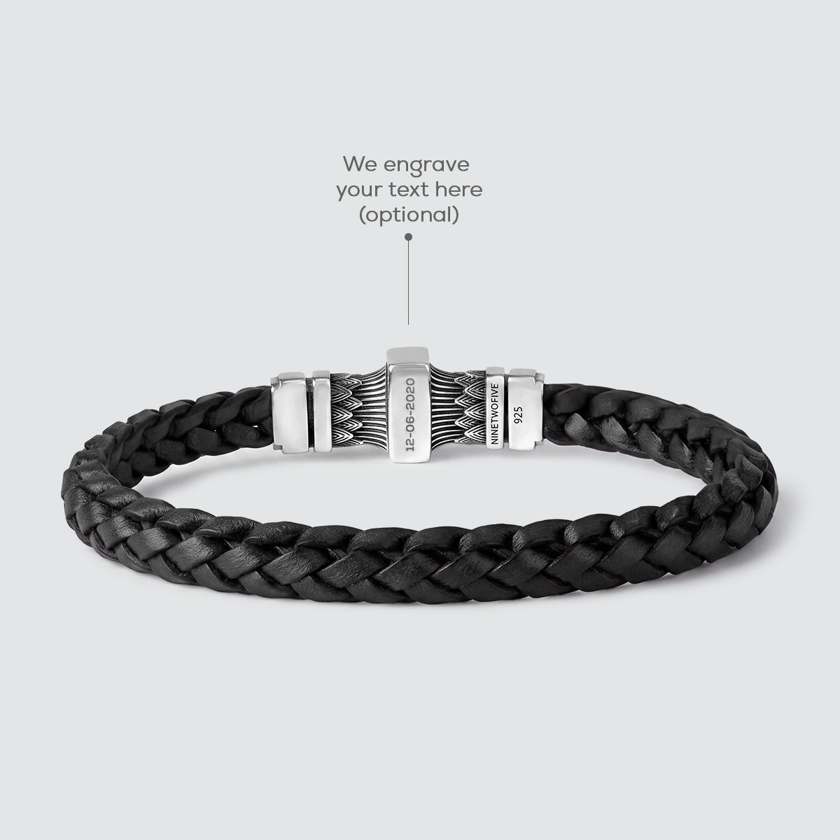A dark brown braided leather bracelet with a silver-toned metal clasp, shown on a light gray background with an overlay pointing to the clasp and the text 'We engrave your text here'.