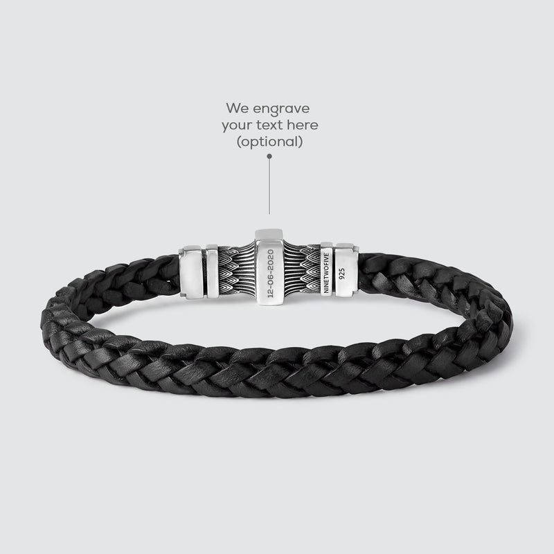 Een donkerbruine, gevlochten leren armband met een zilverkleurige metalen sluiting, afgebeeld op een lichtgrijze achtergrond met een overlay die naar de sluiting wijst en de tekst ‘Hier graveren we jouw tekst’.