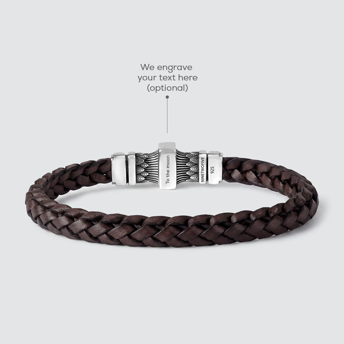 A dark brown braided leather bracelet with a silver-toned metal clasp, shown on a light gray background with an overlay text pointing to the clasp for personalization.