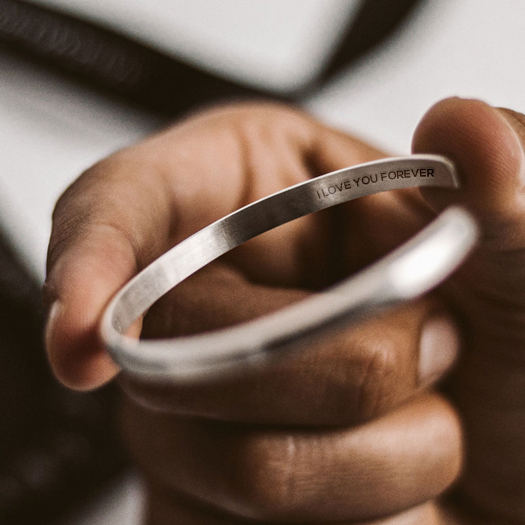 A person holding up a silver bangle with a quote.
