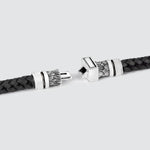 A close-up of a black braided leather bracelet with ornate silver-toned metal end caps, shown on a light gray background.