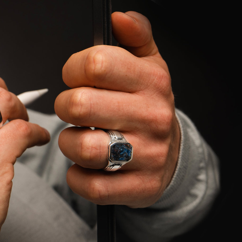 A man is holding a ring with a blue stone.