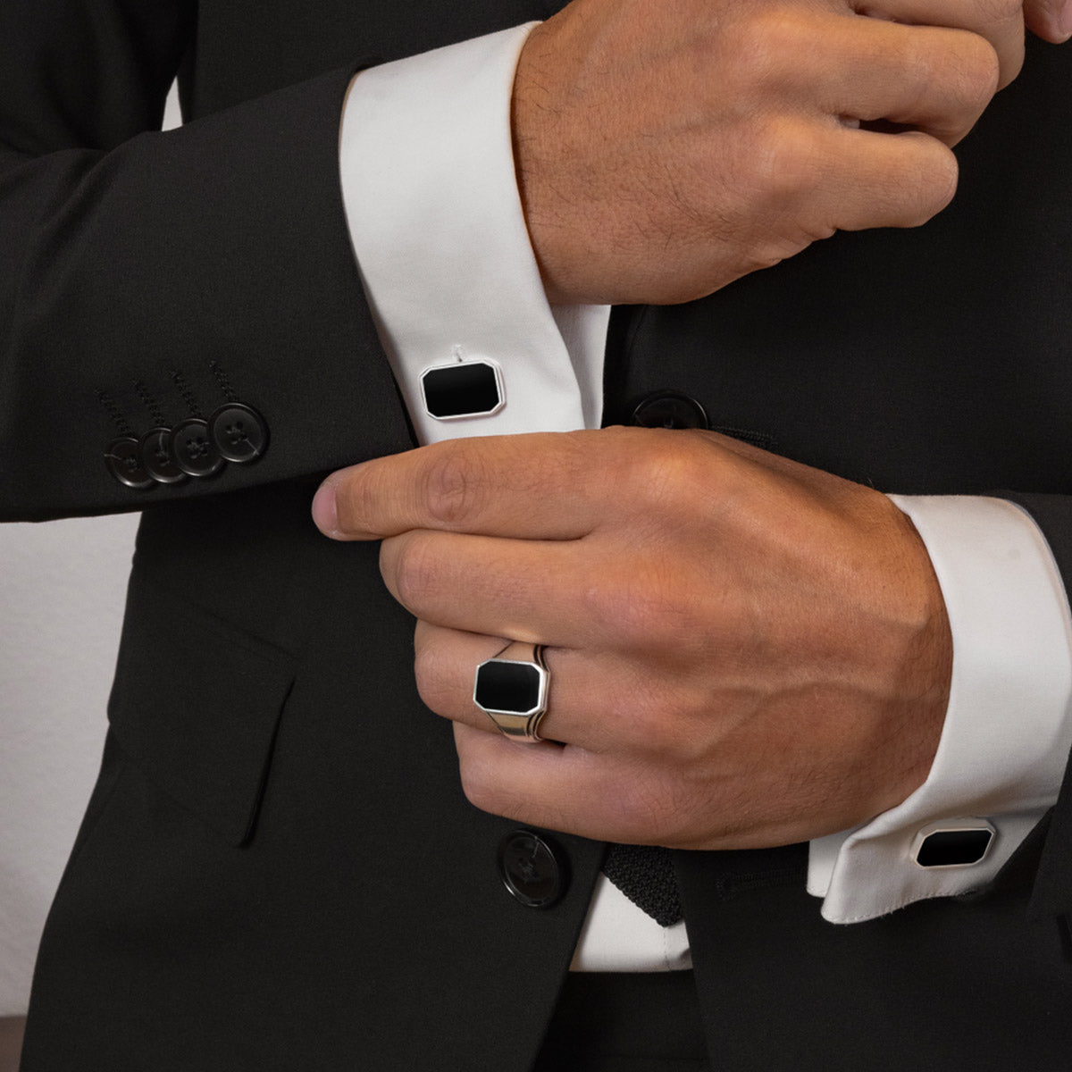 Model in een zwart pak draagt Rael Black Onyx manchetknopen met een zilveren ring van Ninetwofive.