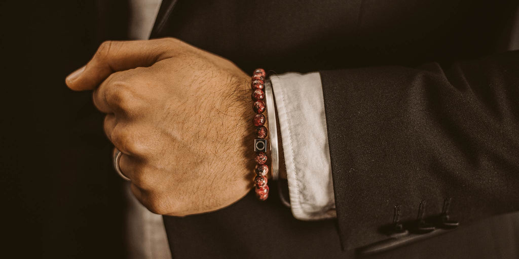 A man in a suit is wearing a red bracelet.