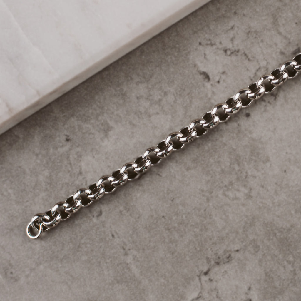 Un bracelet en chaîne en argent posé sur une bille.