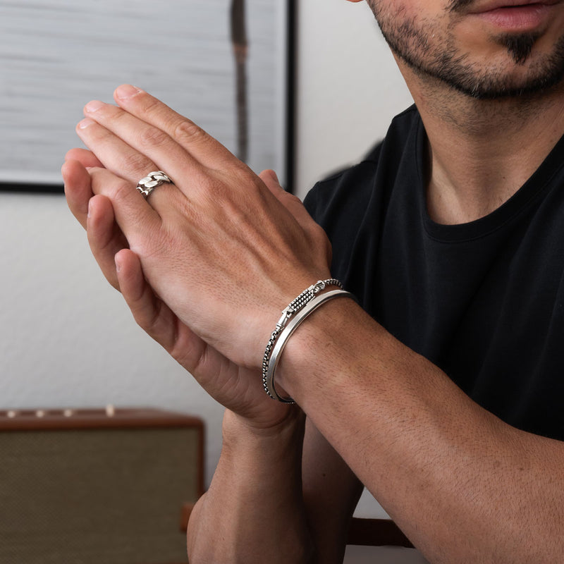 Mann, der silberne Ringe und silberne Box-Chain-Armbänder an den Händen trägt, vor einem neutralen Hintergrund