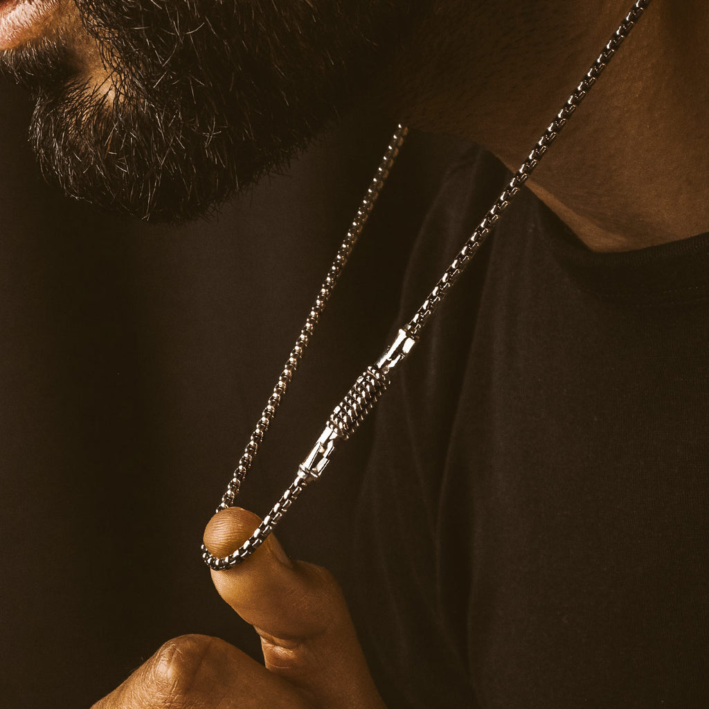 Een man draagt een Kamal - Sterling Zilver Box ketting  3mm, handgemaakt met 925 sterling zilver, als aanvulling op zijn stijlvolle zwarte baard.